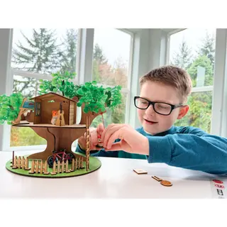 A smiling boy beside the wooden tree house he painted and built