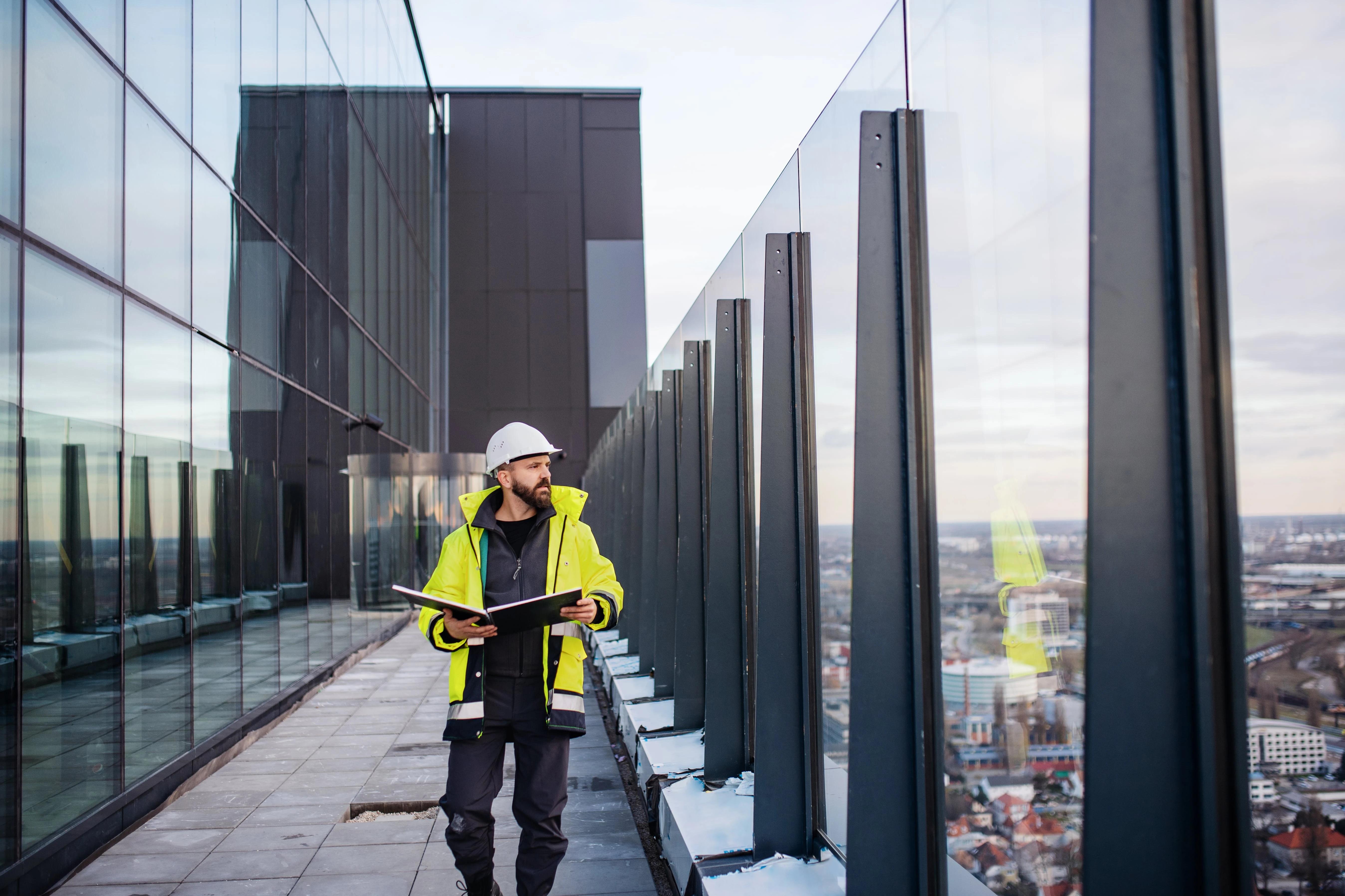 Ingeniør i vernevest går langs glassrekkverket på et tak med utsikt over byen
