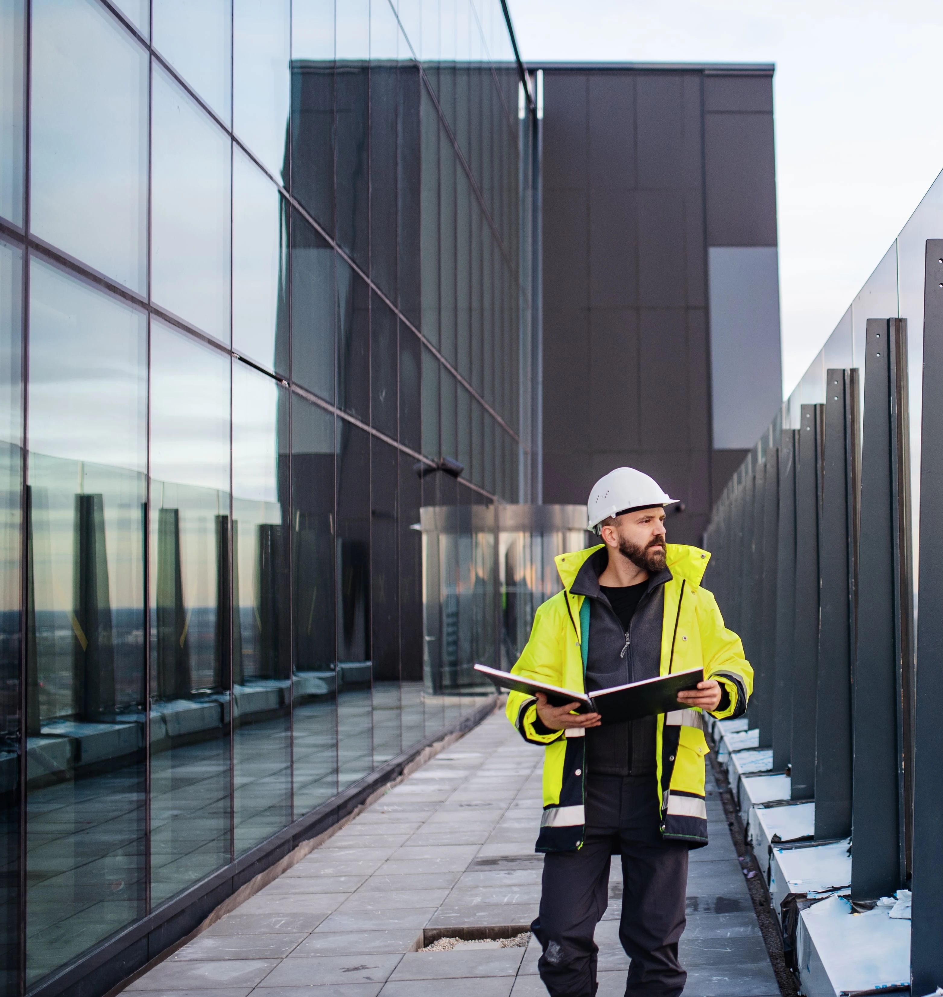 Ingeniør i vernevest går langs glassrekkverket på et tak med utsikt over byen