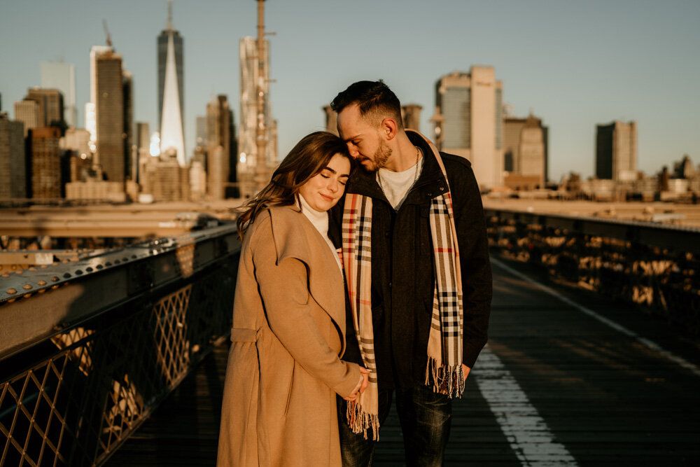 Couple snuggling on brooklyn bridge at sunrise during engagement session