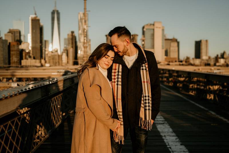Couple snuggling on brooklyn bridge at sunrise during engagement session