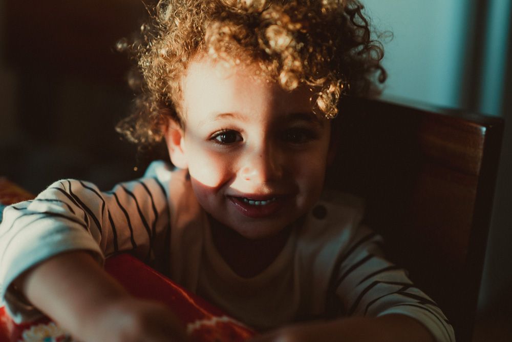 Kid with harsh light and shadows on his face looks at photographer