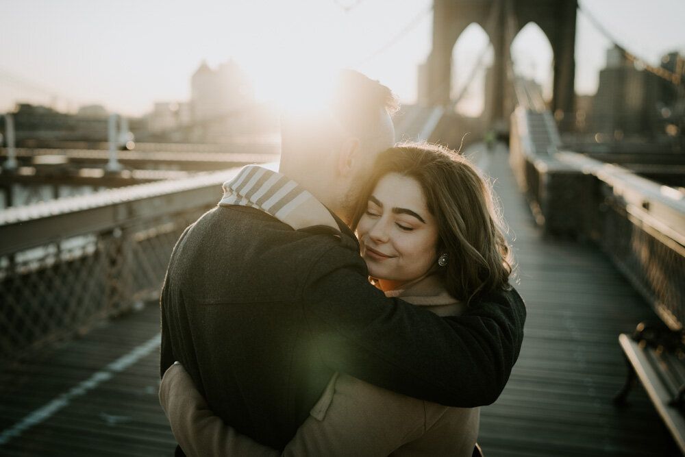 Couple snuggling on brooklyn bridge at sunrise during engagement session