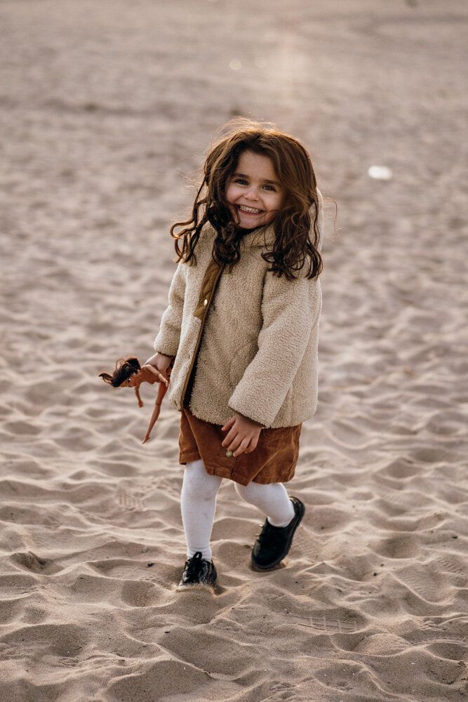 Young girl smiles at photographer during family session at coney island beach
