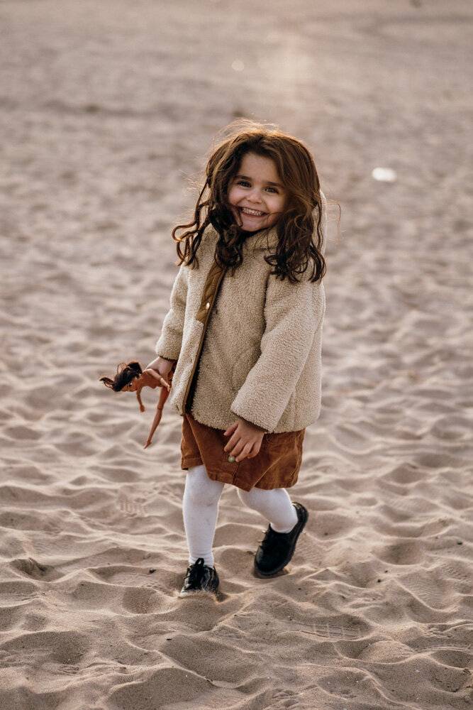 Young girl smiles at photographer during family session at coney island beach