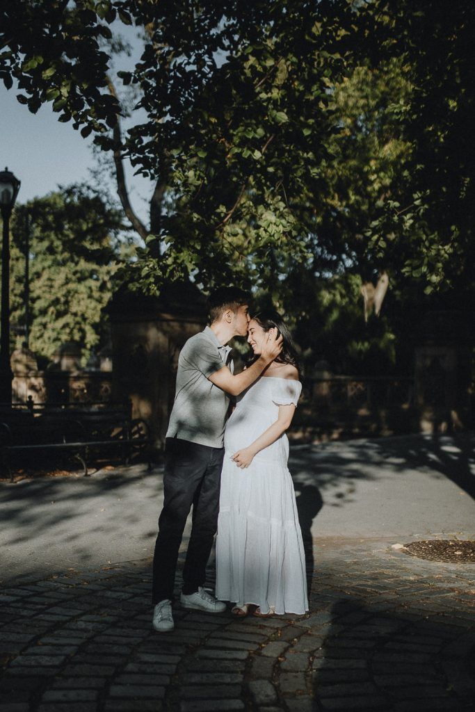 Expecting couple snuggling in central park during maternity photoshoot