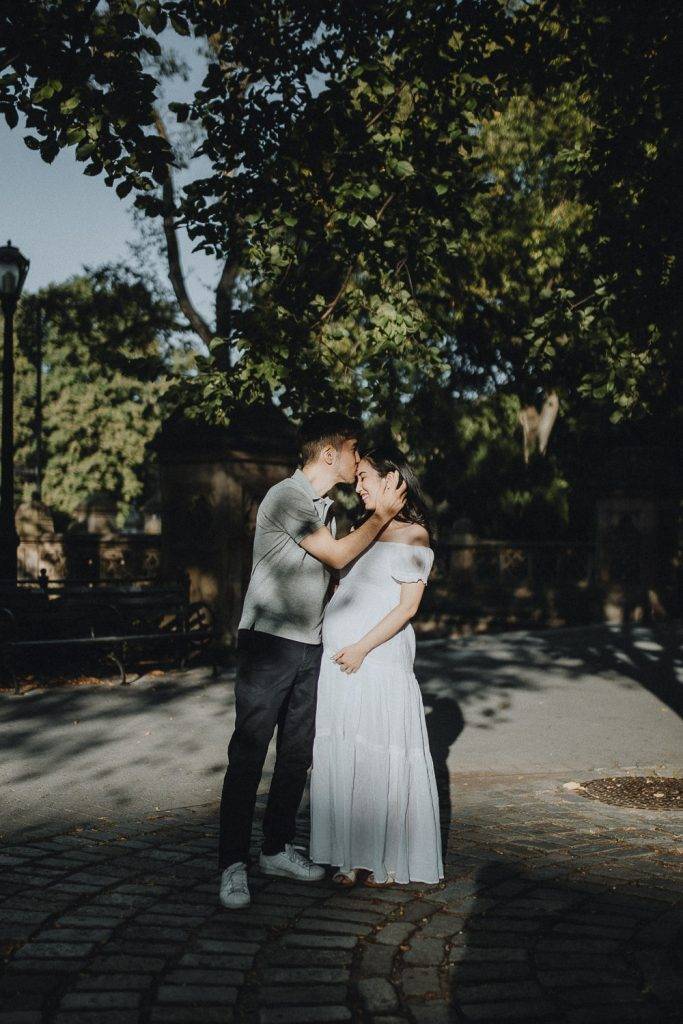 Expecting couple snuggling in central park during maternity photoshoot