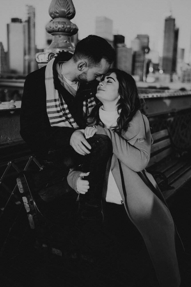 Couple snuggling on park bench during brooklyn bridge engagement session