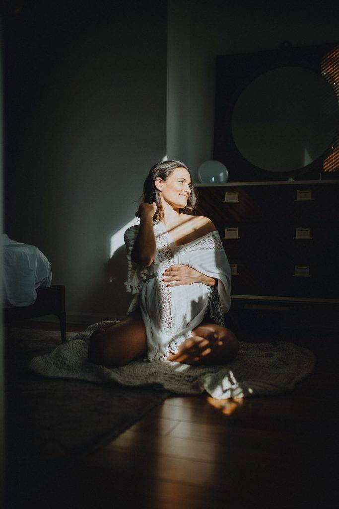 Pregnant woman in light and shadows during maternity photoshoot in brooklyn home