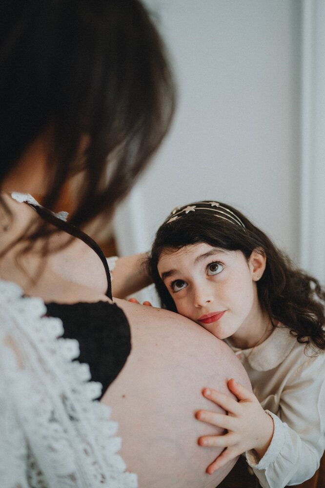 Girl holds pregnant mother's belly during in home family session