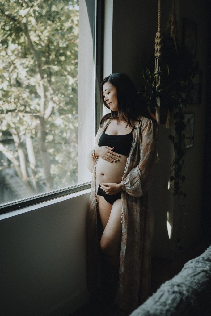 Pregnant woman standing by window during maternity session in brooklyn