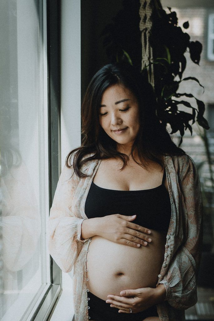 Pregnant woman standing by window during maternity session in brooklyn