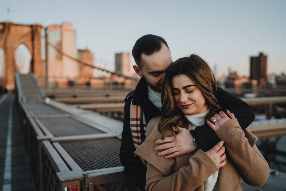 Couple snuggling on brooklyn bridge during engagement session