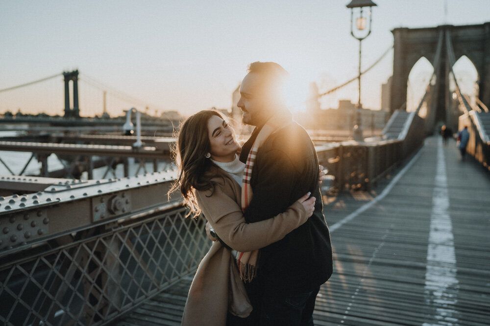 Couple snuggling on brooklyn bridge at sunrise during engagement session