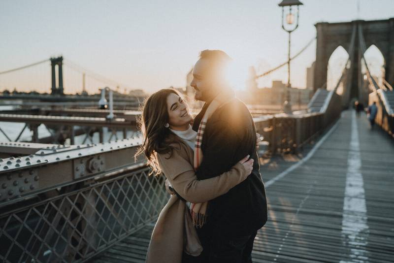Couple snuggling on brooklyn bridge at sunrise during engagement session