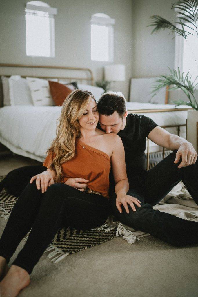 Couple cuddles by bed during in home session in brooklyn