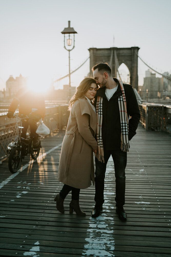 Couple snuggling on brooklyn bridge at sunrise during engagement session