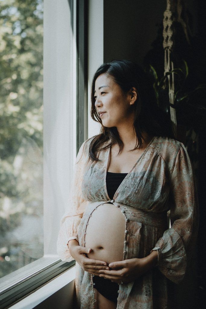 Pregnant woman standing by window during maternity session in brooklyn