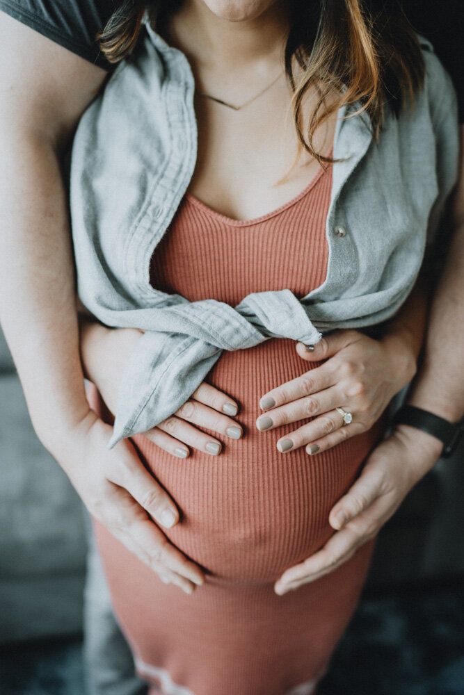 Expecting couple touches baby bump during in home maternity session in brooklyn