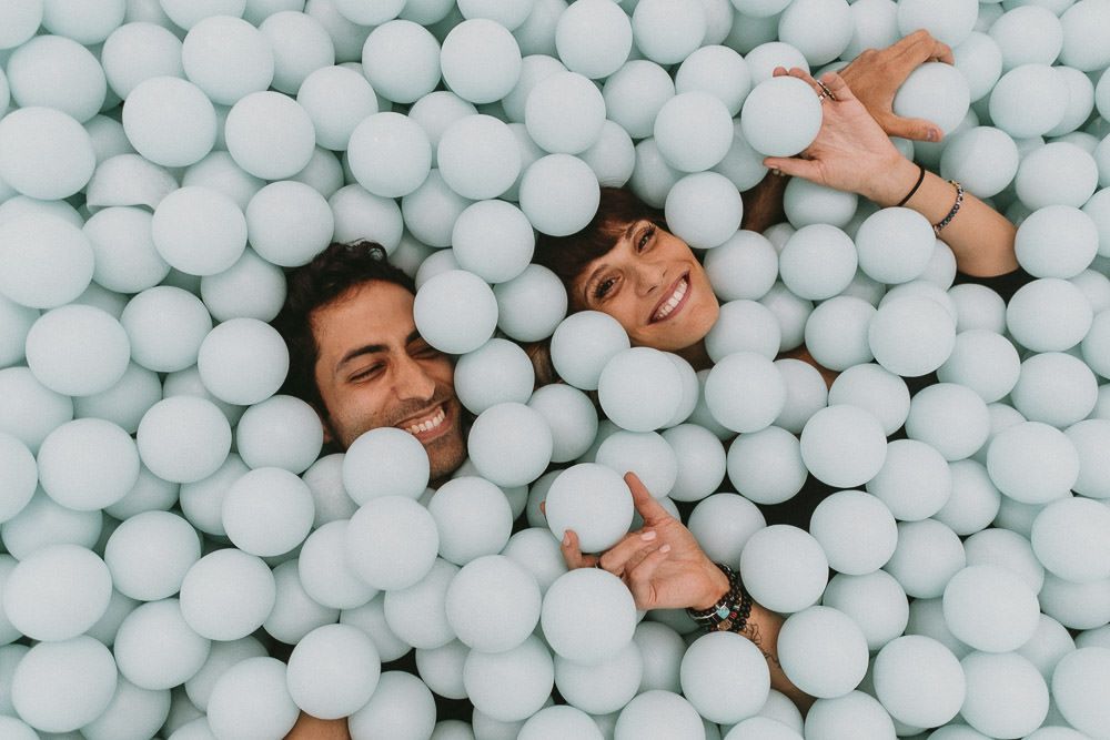 Couple in giant blue ball pit laughing during fun nyc engagement session