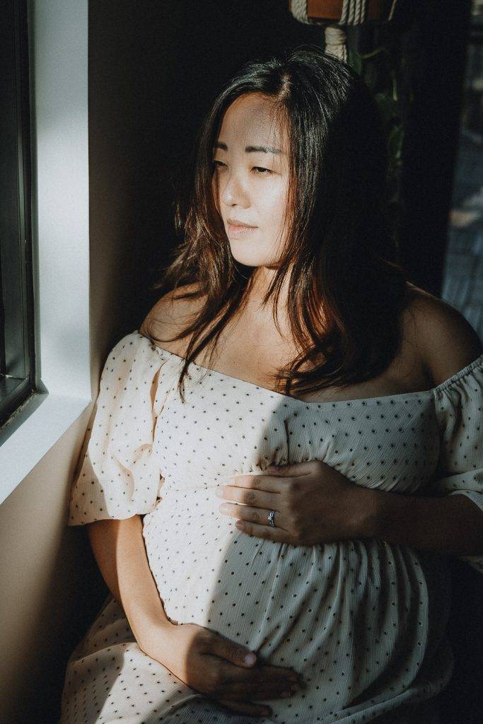 Pregnant woman in patch of light by window during maternity session