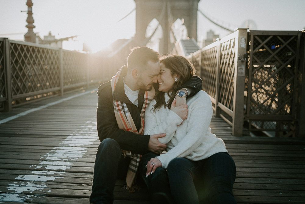 Couple snuggling on brooklyn bridge at sunrise during engagement session