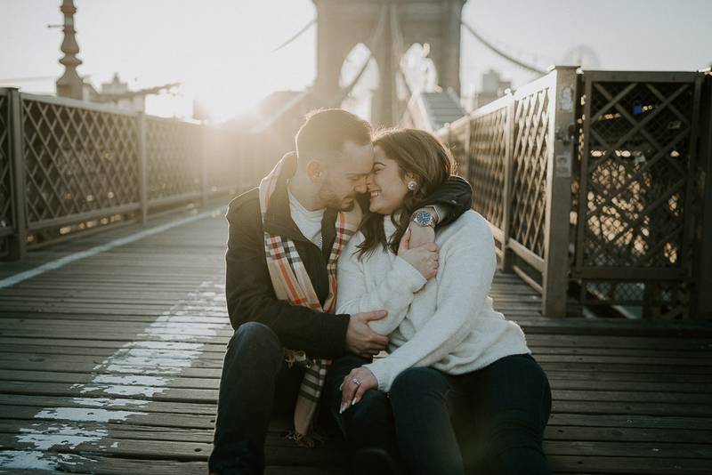 Couple snuggling on brooklyn bridge at sunrise during engagement session