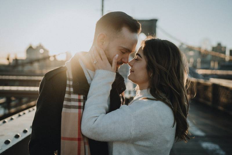 Couple snuggling on brooklyn bridge at sunrise during engagement session