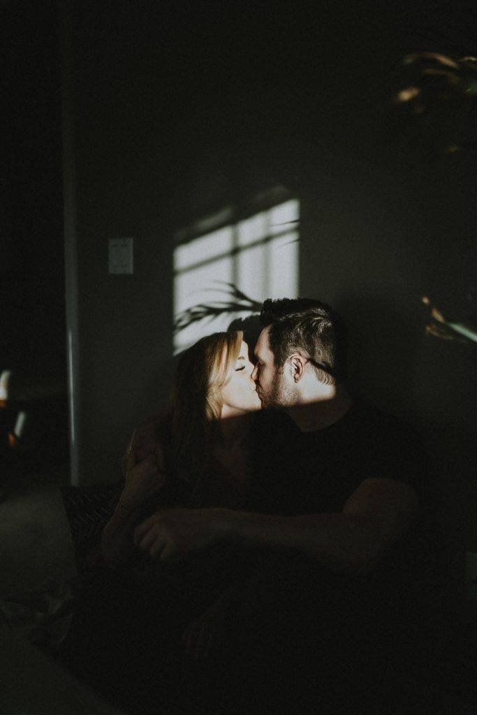 Couple kissing in patch of harsh light and shadows during in home session