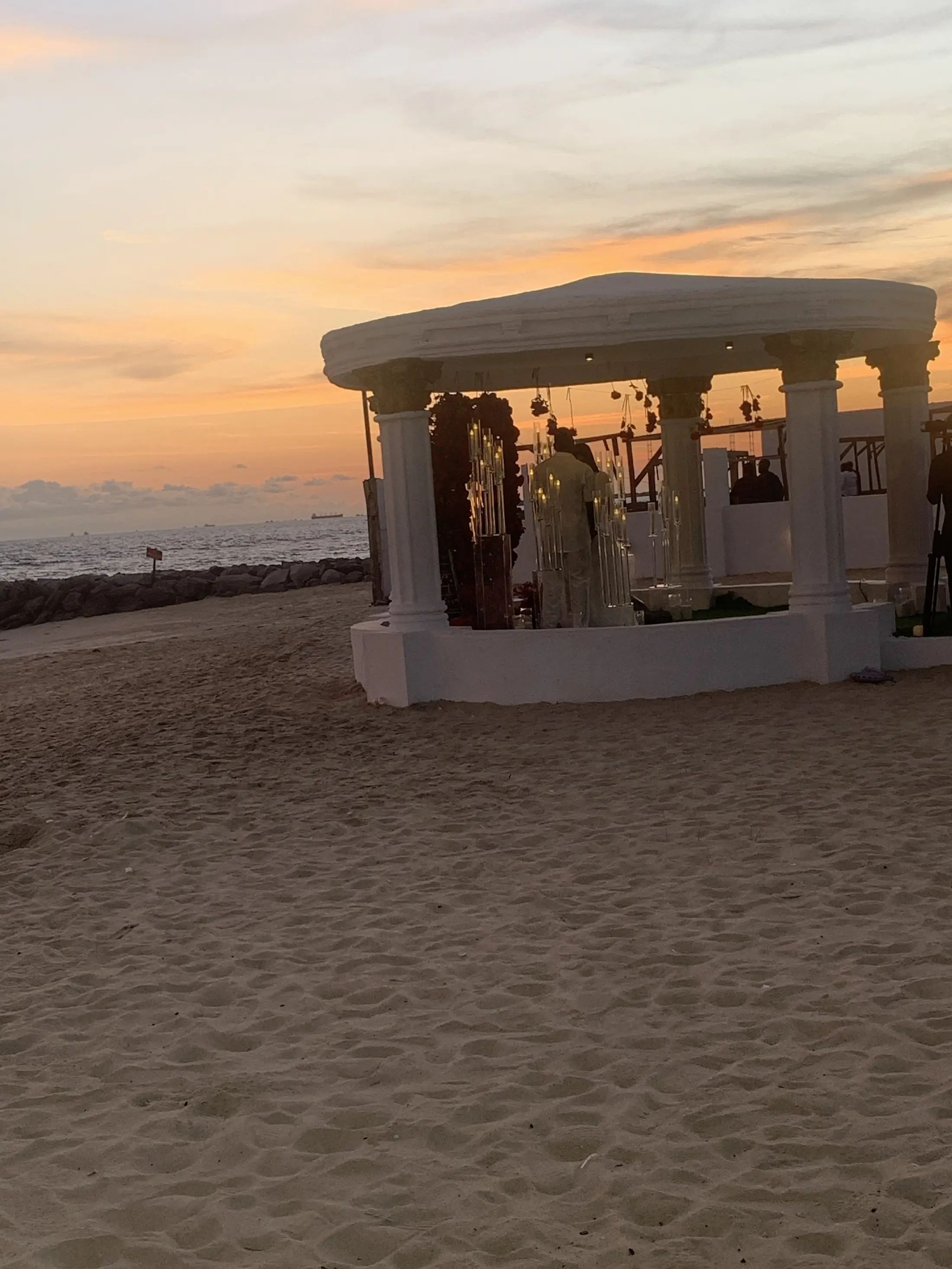The gazebo at sunset with guests gathered, the sky orange over the sea