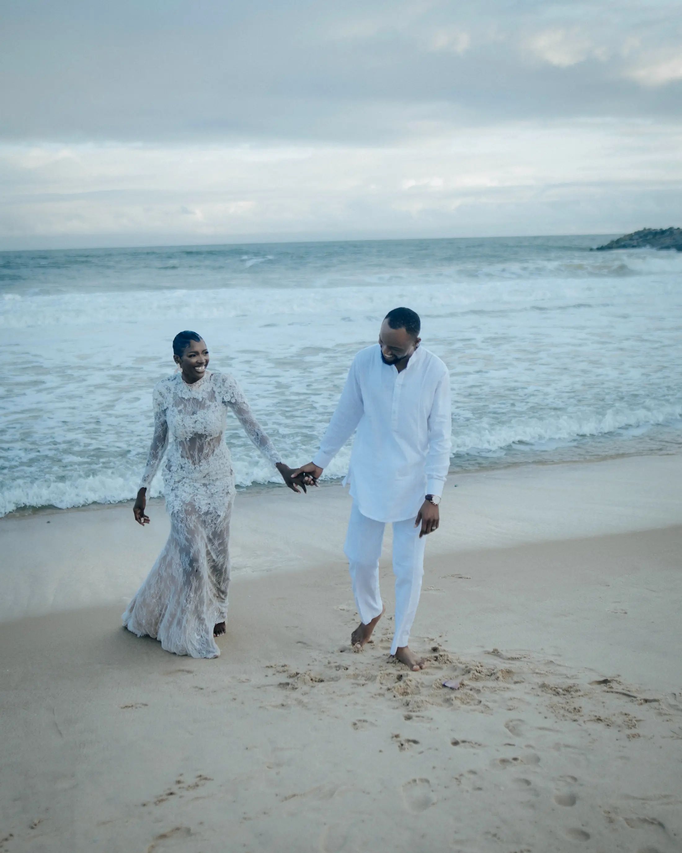 A bride and groom walking hand in hand along the shore