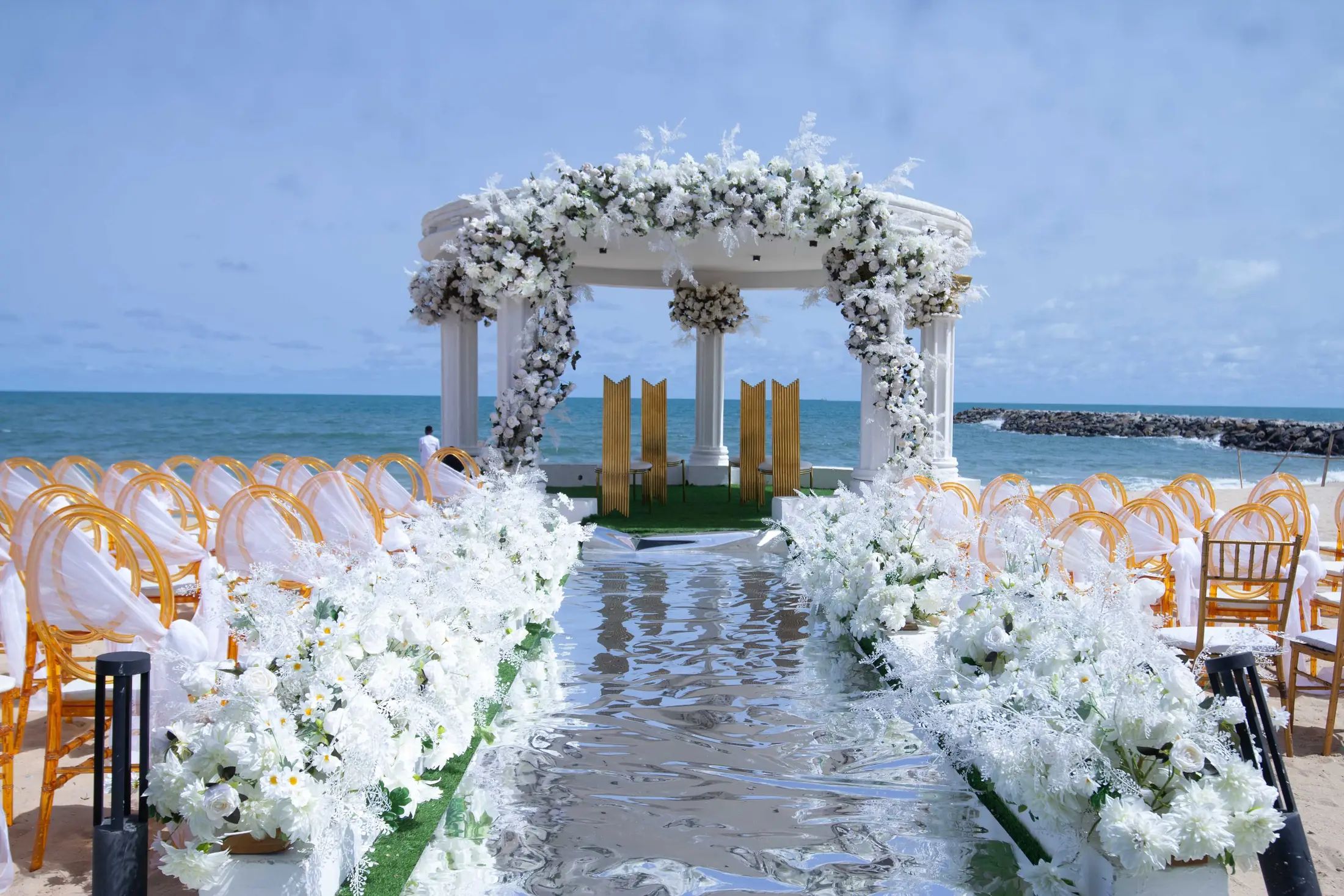 Looking down the white aisle to the flowered gazebo, the sea beyond