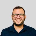 Homem branco de cabelo castanho e barba bem feita, usa óculos e camisa azul marinho com gola