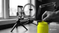 A phone on a mini tripod with a ring light films a desk while a hand drops a coin into a yellow jar