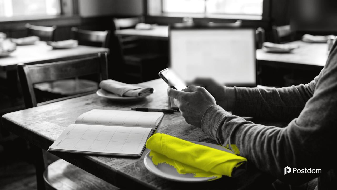 How to schedule Facebook posts: a restaurant owner holds a phone at a table with an open weekly planner and a yellow napkin on a plate