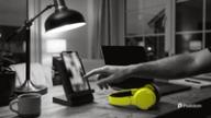 How to schedule YouTube Shorts: a creator taps a phone standing upright in a desk stand next to yellow headphones and a laptop in the evening