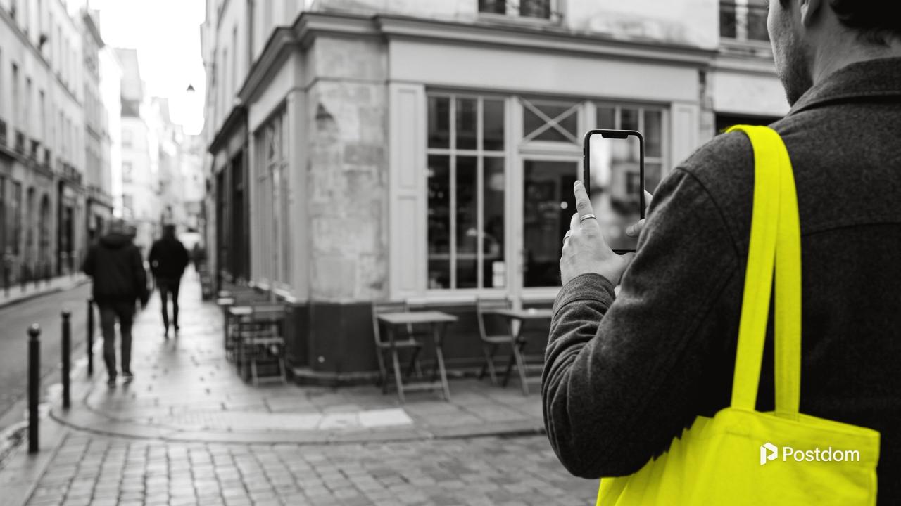 A person seen from behind films a small corner cafe on their phone from the pavement.