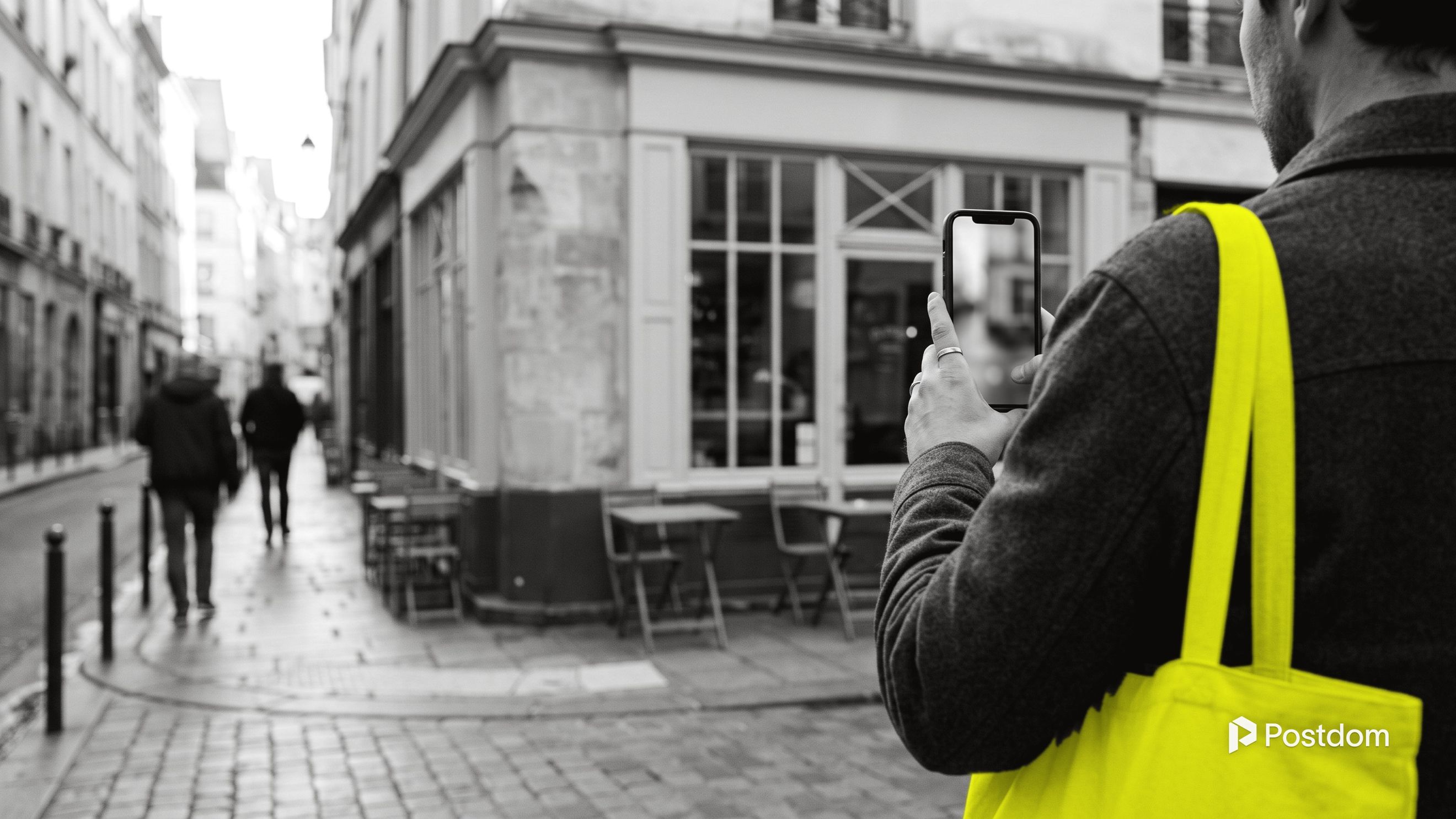 A person seen from behind films a small corner cafe on their phone from the pavement.