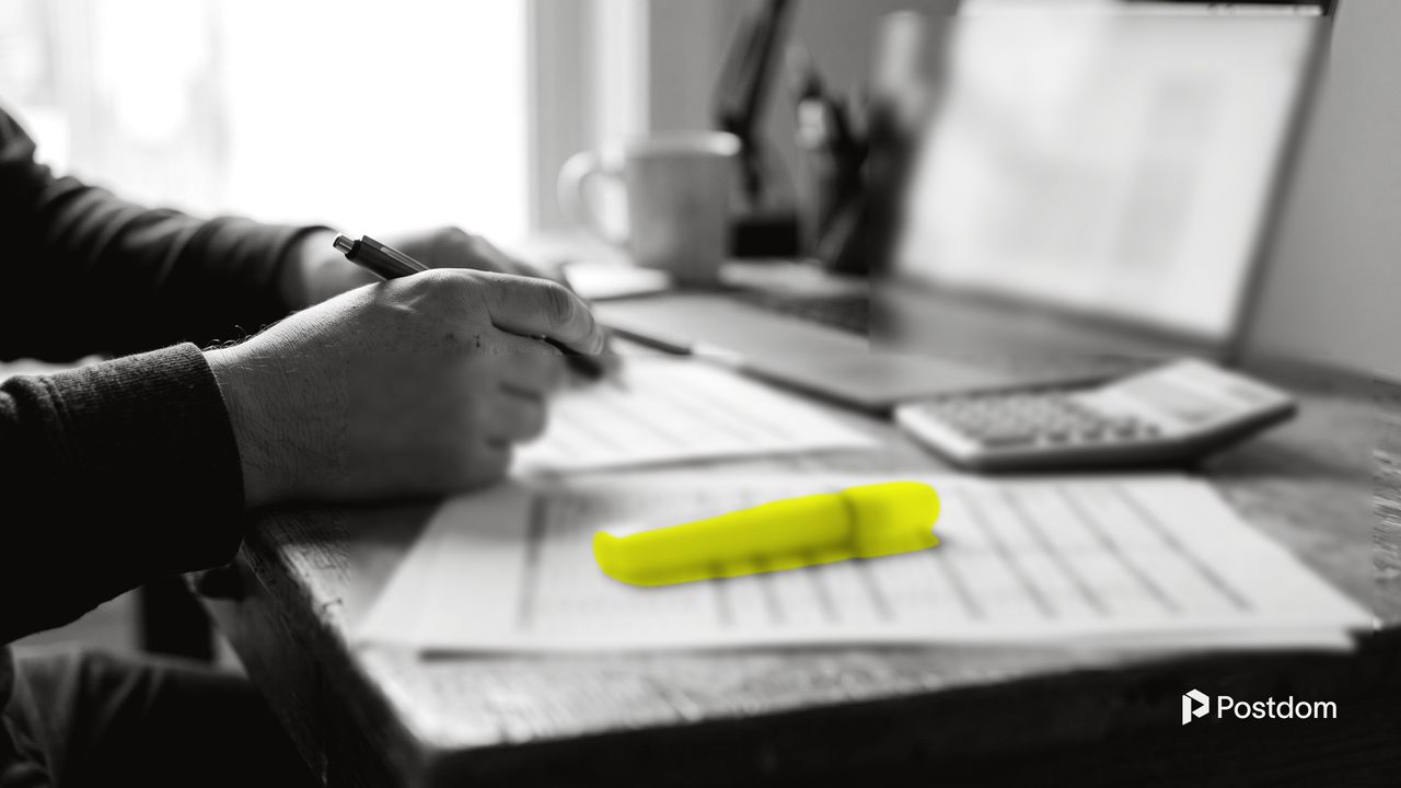 AI social media tools pricing: a business owner compares printed price sheets with a pen, a calculator and a yellow highlighter beside a laptop