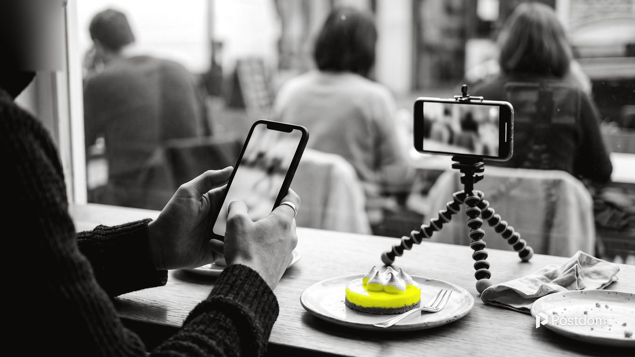TikTok trends: a café customer scrolls a phone at a window table while a second phone on a small tripod is set up to film a yellow lemon tart