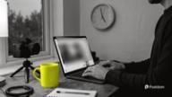Best time to post on YouTube: a creator edits a video on a laptop next to a camera on a small tripod and a yellow mug, a wall clock near five behind