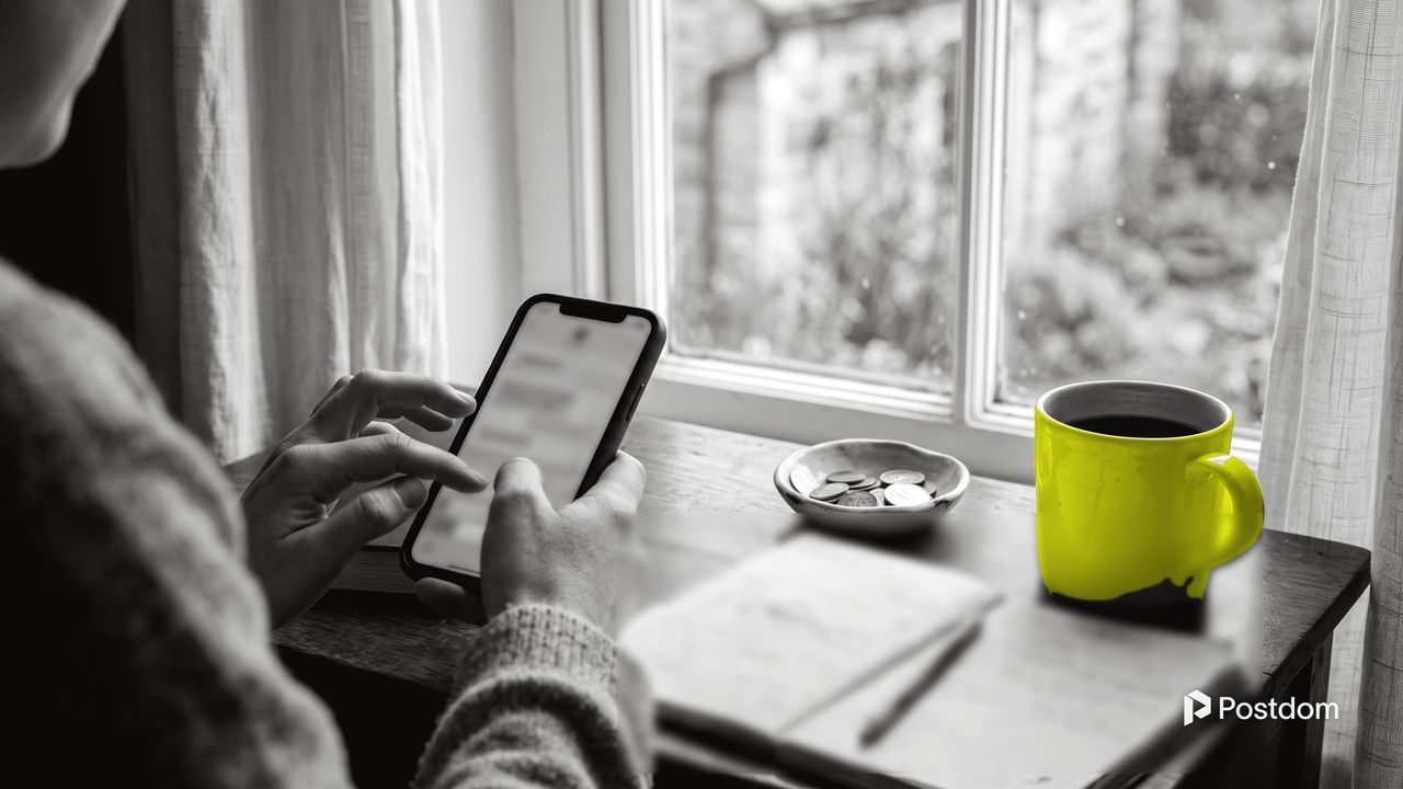 How to make money on Twitter: a person types a post on a phone at a window desk with a notebook, a dish of coins and a yellow mug