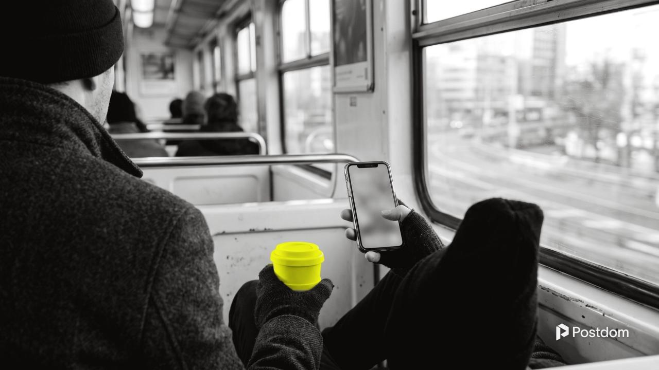Best time to post on Twitter: a commuter on a morning train holds a phone and a yellow reusable coffee cup by the window