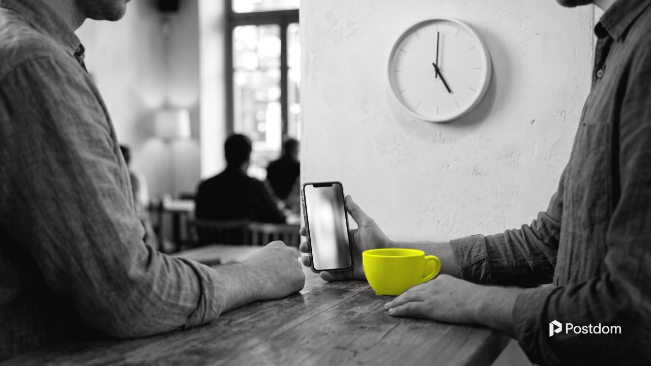 The best time to post on TikTok: two people at a cafe counter at five o'clock, one holding a phone ready to post, with a yellow cup in front and a wall clock behind