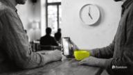 The best time to post on TikTok: two people at a cafe counter at five o'clock, one holding a phone ready to post, with a yellow cup in front and a wall clock behind