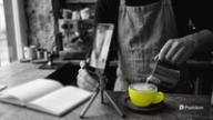 Schedule Instagram Reels: a barista films latte art being poured into a yellow cup with a phone on a small tripod, an open weekly planner beside it