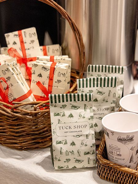 Interior view of a retail clothing store displaying merchandise on racks and shelves, with wrapped gift boxes and various items arranged on a table in the foreground.