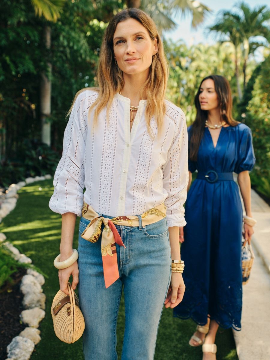 woman walking outside wearing white eyelet blouse with jeans and printed scarf as belt