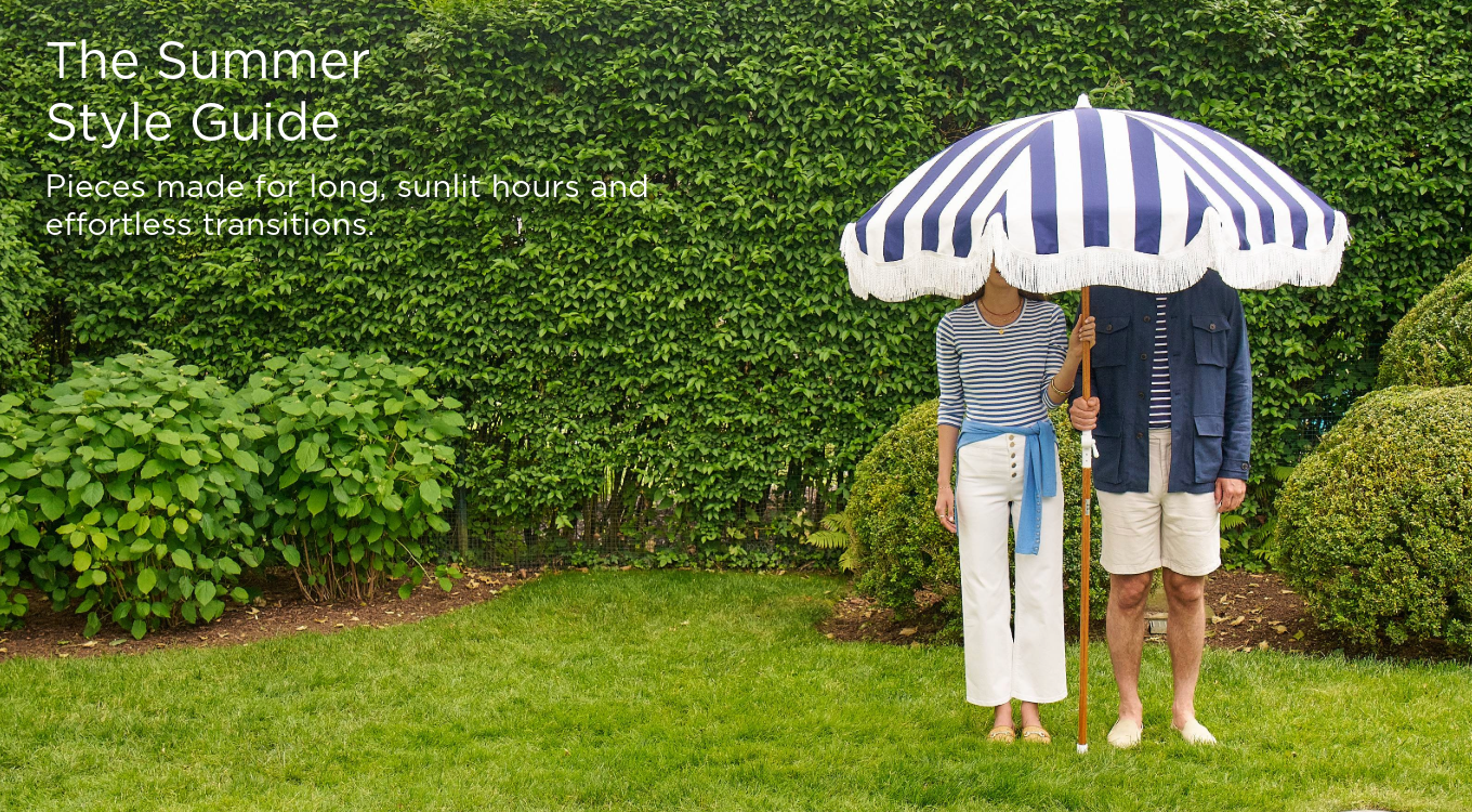 man and woman standing outside in navy and white outfits holding a blue and white stripe umbrella