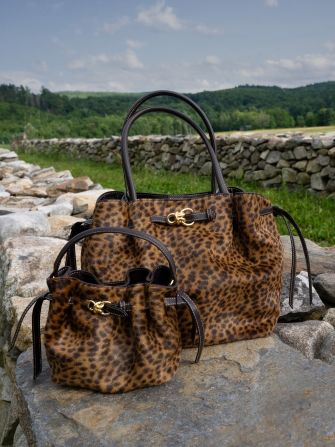 A large and small leopard print handbag sitting on a stone wall outdoors.